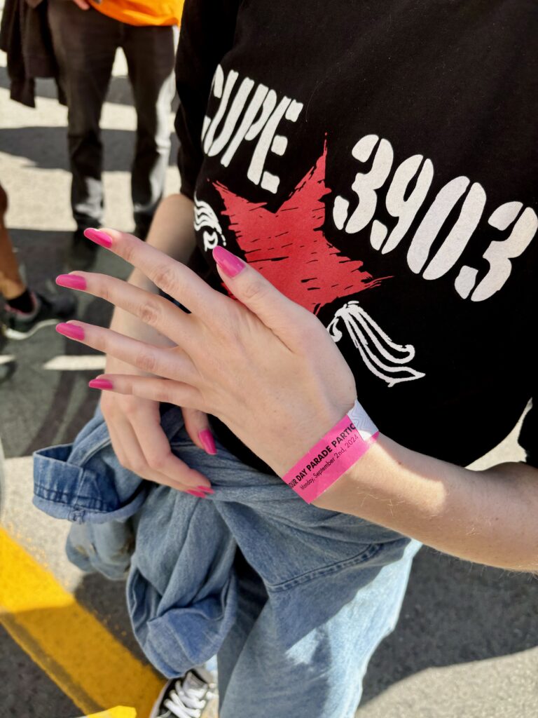 A member wearing a CUPE 3903 shirt, showing off their hot pink nails, which matches their CNE admittance bracelet.